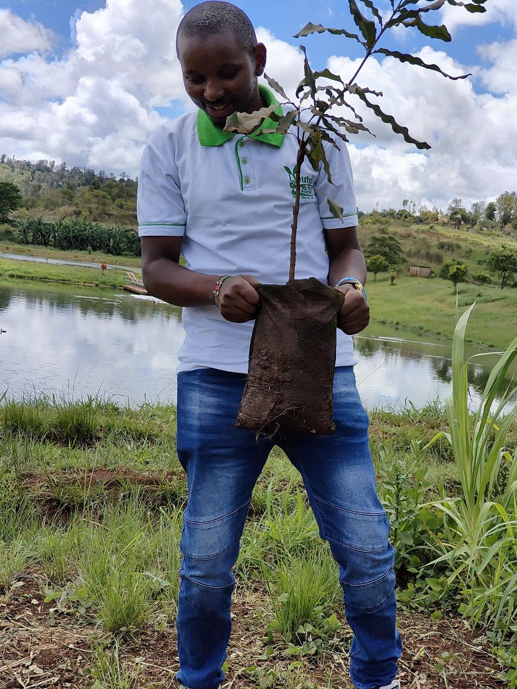 A man holding a tree seedling beside a pond at the MUWASCO Sewerage Treatment site